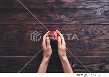 Woman's hands holding one apple on dark background Woman's hands holding one apple on dark background 44707803