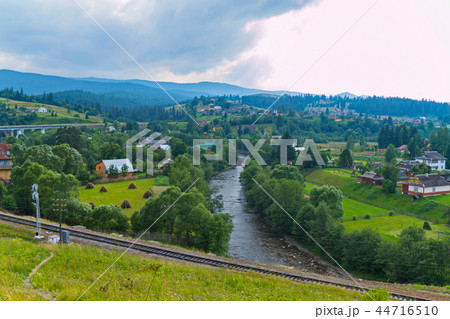 village on a green plain with a railway and a moun village on a green plain with a railway and a moun 44716510