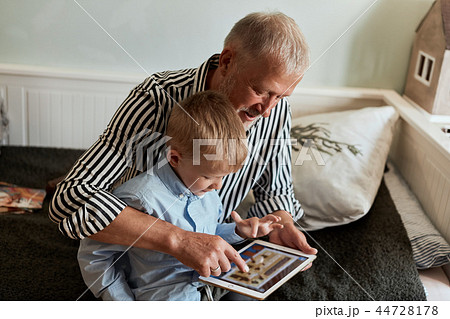 Grandfather and grandson using digital tablet while sitting on couch 44728178