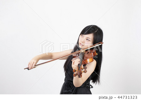 白い背景の前でヴァイオリンを弾いている黒髪の若い女性 44731323