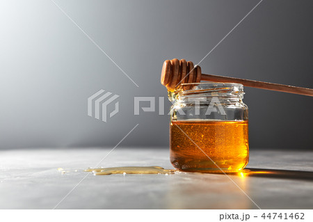 Wooden honey spoon above on a glass jar full natural organic syrup in a glass pot on a gray stone 44741462