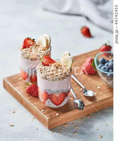 Granola, halves of strawberries, banana, chia seeds with yogurt in a glasses on a wooden board on a 44742455