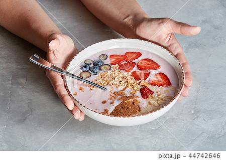 Woman hands hold bowl with appetizing healthy granola dessert with pieces of strawberries, cream Woman hands hold bowl with appetizing healthy granola dessert with pieces of strawberries, cream 44742646