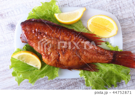 Smoked fish and lemon on green lettuce leaves on Wooden cutting board isolated on white background. 44752871