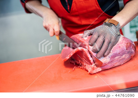 Woman cutting fresh meat in a butcher shop with metal safety mes Woman cutting fresh meat in a butcher shop with metal safety mes 44761090