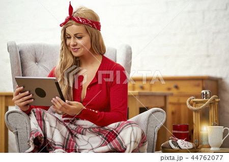 young beautiful woman in an armchair with a tablet wrapped in a blanket during Christmas time 44762077