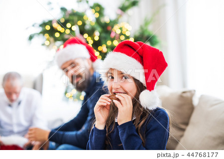 A small girl with Santa hat and her father and grandfather sitting on a sofa at Christmas time. A small girl with Santa hat and her father and grandfather sitting on a sofa at Christmas time. 44768177