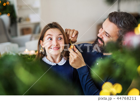 Small girl standing by a Christmas tree with her father at home, having fun. 44768211