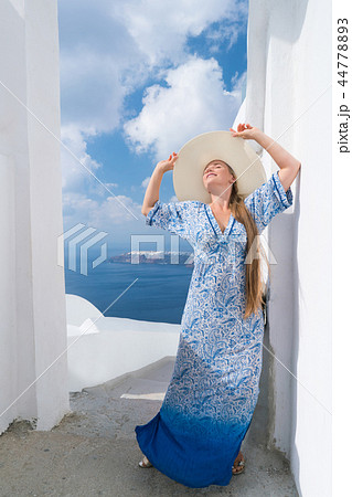 young woman in a white and blue dress enjoys a walk around Santorini 44778893