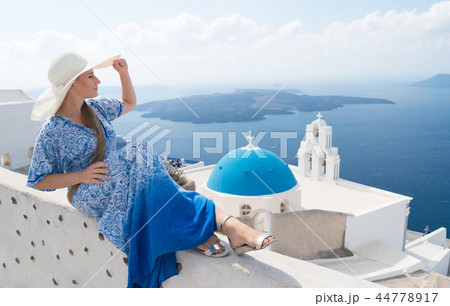 young woman in a white and blue dress enjoys a walk around Santorini 44778917