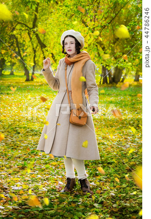 Girl in autumn on walk looks at the falling leaves 44786246