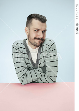 Serious suspicious business man sitting at a table on a blue background Serious suspicious business man sitting at a table on a blue background 44807770