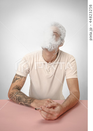 Handsome hipster man smoking cigarette at home. Man looking upwards and enjoying spending free time. 44823256