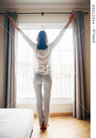 Full length portrait of happy woman stretching near window after 44827089