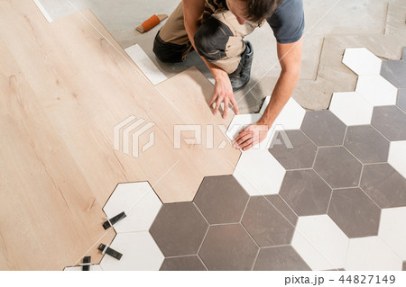 Male worker installing new wooden laminate flooring. The combination of wood panels of laminate and Male worker installing new wooden laminate flooring. The combination of wood panels of laminate and 44827149