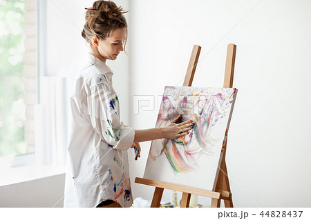 Woman artist smearing oil paints by hands on canvas picture 44828437