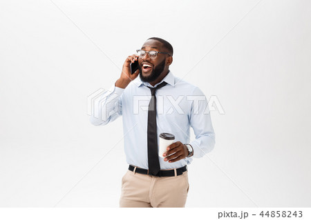 Good talk. Cheerful young African man in white shirt holding a cup of coffee and talking on the 44858243