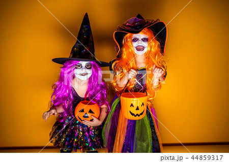 Two Beautiful girl in a witch costume on a yellow background scaring and making faces 44859317