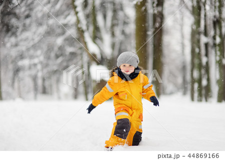 Cute little boy in yellow winter clothes walks during a snowfall 44869166