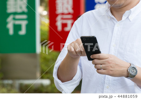 金融イメージ　銀行の看板とスマートフォンを操作する男性 44881059