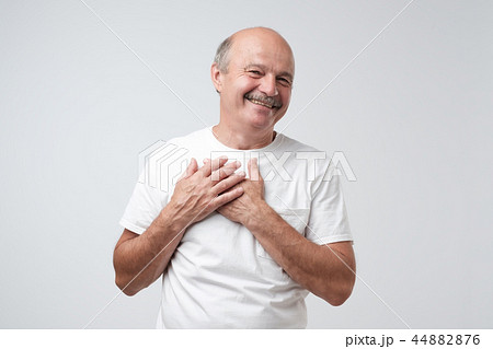 Cheerful man smiles happily, keeps hands on chest. 44882876