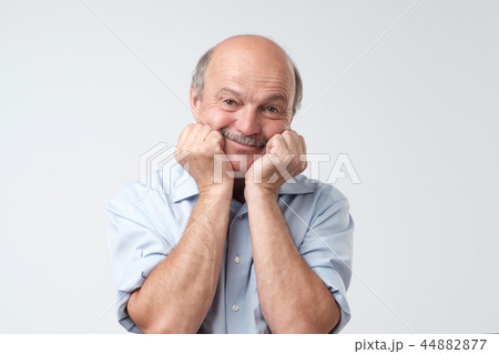 Portrait of cute bald caucasian male holding hands on cheeks, smiling and glancing at camera Portrait of cute bald caucasian male holding hands on cheeks, smiling and glancing at camera 44882877