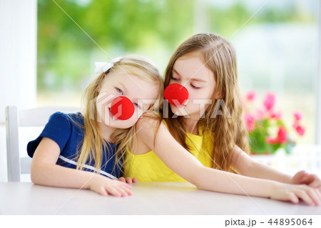 Happy little sisters wearing red clown noses having fun together on sunny summer day at home 44895064