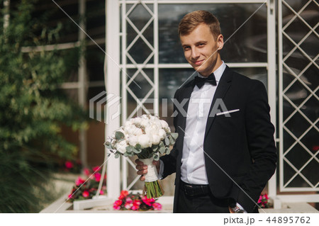 Happy groom in stylish suit take brides bouquet and smile Happy groom in stylish suit take brides bouquet and smile 44895762