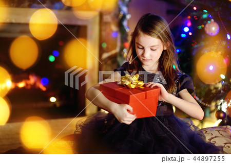 Happy girl opening Christmas gifts by a fireplace 44897255
