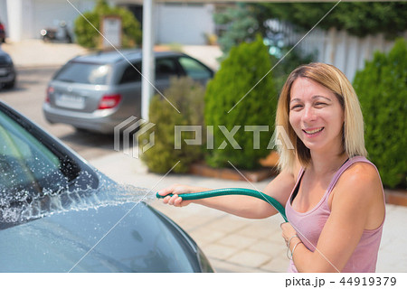 Young woman washing car with hose. Car detailing. Young woman washing car with hose. Car detailing. 44919379