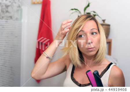 Beautiful blond girl using hair iron at home 44919408