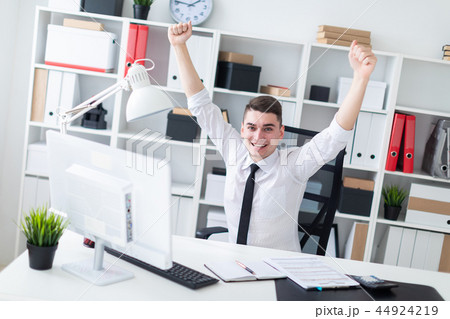A young man sitting at a computer Desk in the office and raised his hands up. A young man sitting at a computer Desk in the office and raised his hands up. 44924219
