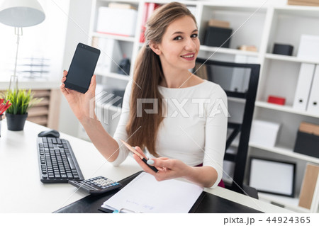 A young girl sitting at a table and holding a phone. 44924365