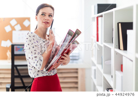A young girl standing in the office, talking on the phone and holding a folder with documents. 44924976