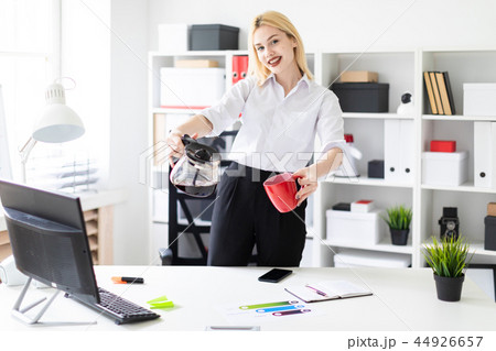 A young girl standing in the office and holding a Cup and a coffee pot. 44926657