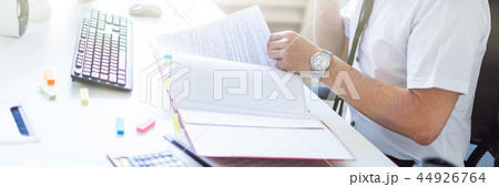 A man is sitting in the office, working with documents, holding a marker in his mouth and talking on A man is sitting in the office, working with documents, holding a marker in his mouth and talking on 44926764