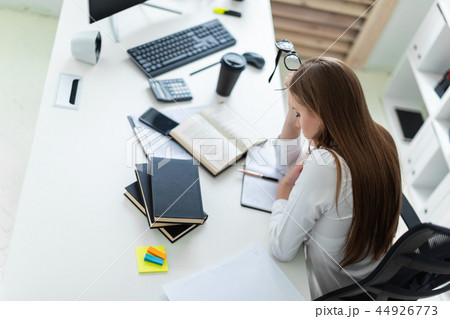 A young girl holding glasses and working in the office with books and documents. A young girl holding glasses and working in the office with books and documents. 44926773