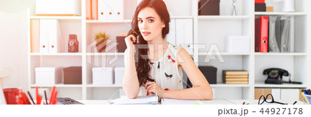 A beautiful young girl sits at the office table, holds her hair in her hand and looks straight. A beautiful young girl sits at the office table, holds her hair in her hand and looks straight. 44927178