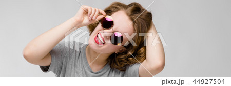 Charming young girl in a gray T-shirt on a gray background. Cheerful girl in round glasses Charming young girl in a gray T-shirt on a gray background. Cheerful girl in round glasses 44927504