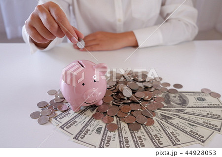 women putting coin in Piggybank with money on desk women putting coin in Piggybank with money on desk 44928053