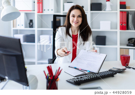 A young girl sitting in the office at a computer Desk and stretches forward a pen and a sheet. A young girl sitting in the office at a computer Desk and stretches forward a pen and a sheet. 44928059