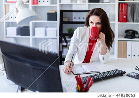 A young girl sitting in the office at the computer Desk and holding a red Cup. 44928063