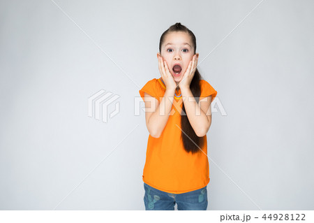 Girl in an orange t-shirt and blue jeans on a gray background 44928122