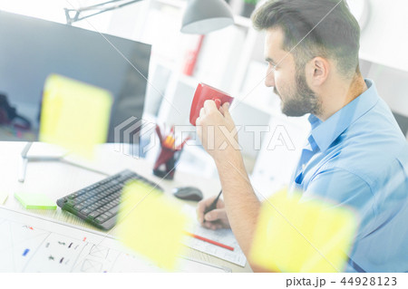 A young man stands in the office near a transparent Board with stickers. A young man stands in the office near a transparent Board with stickers. 44928123