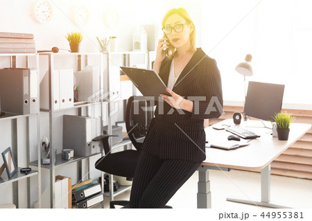 A young girl standing in the office and talking on the phone. A young girl standing in the office and talking on the phone. 44955381