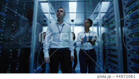 Workers in a data center walking between rows of server racks 44972061