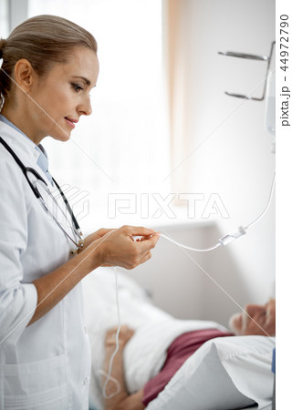 Doctor regulating IV infusion while patient resting on blurred background 44972790