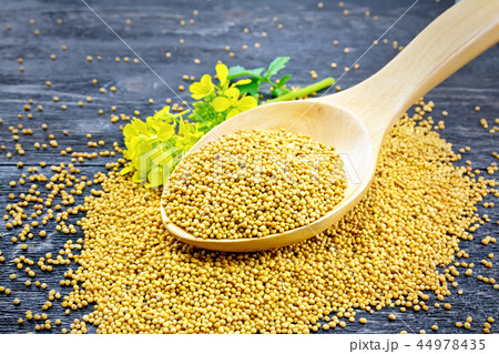 Mustard seeds in wooden spoon with flower on board Mustard seeds in wooden spoon with flower on board 44978435
