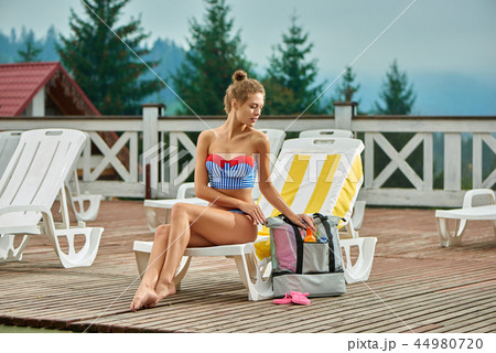 Sweet woman getting sunblock cream from gray backpack. 44980720