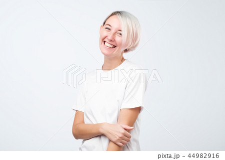 Thoughtful model with short dyed hair dressed in white t-shirt standing in studio. Thoughtful model with short dyed hair dressed in white t-shirt standing in studio. 44982916